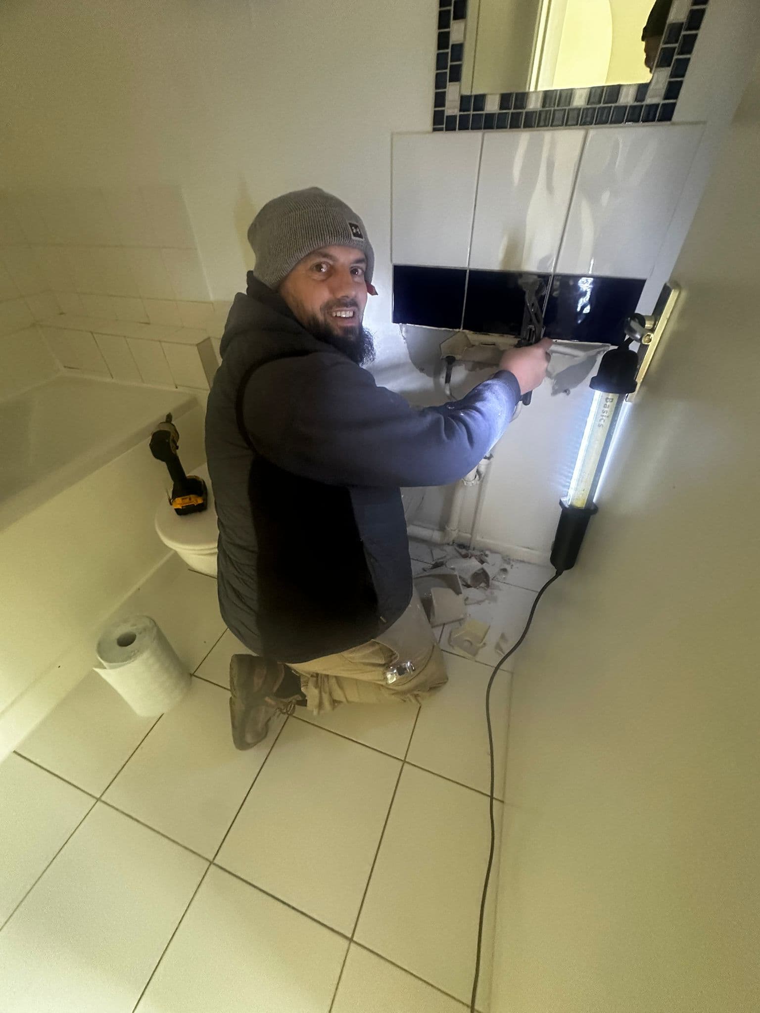 Worker smiling at camera while working on bathroom sink plumbing