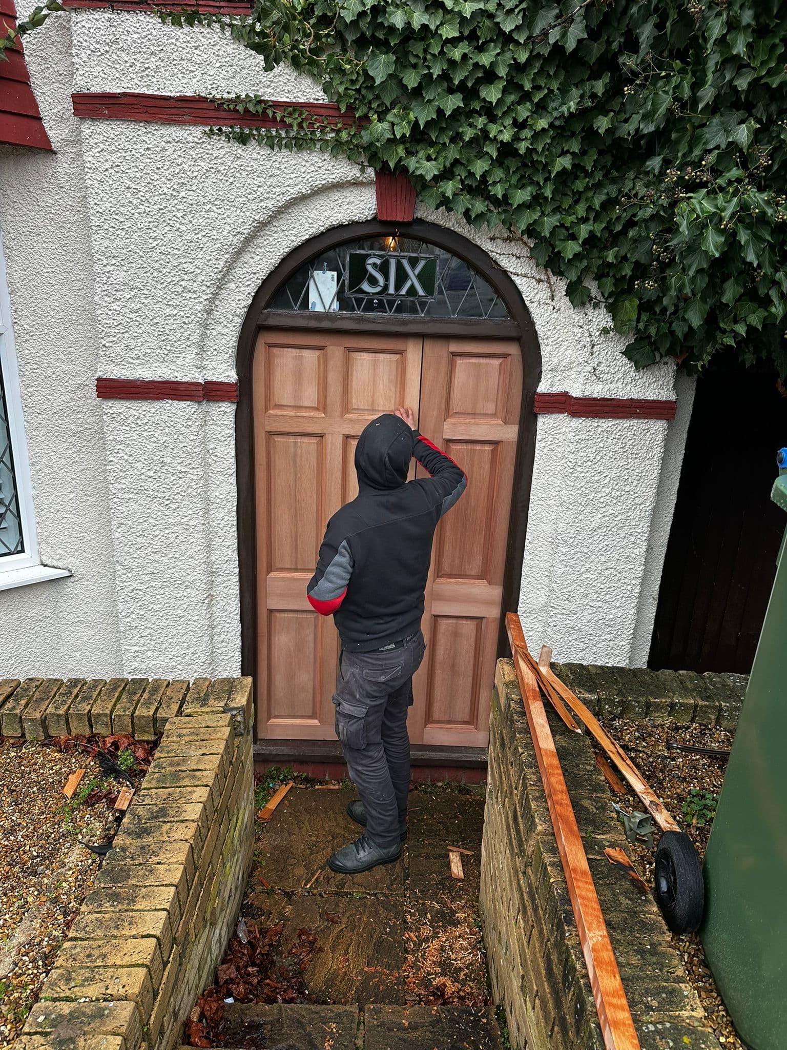 Worker fitting large arched wooden front door marked with house number