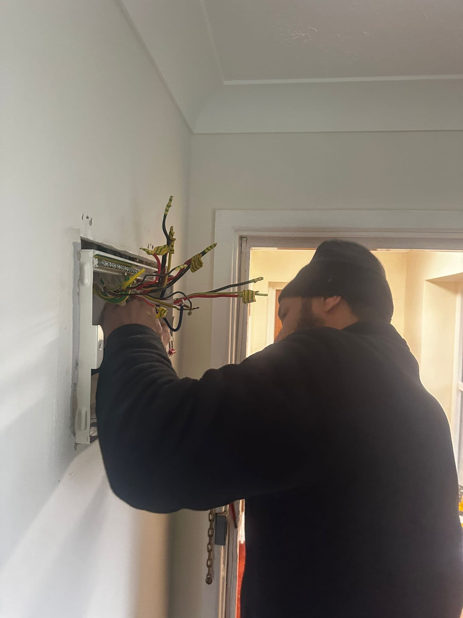 Electrician wiring consumer unit with exposed cables working from behind