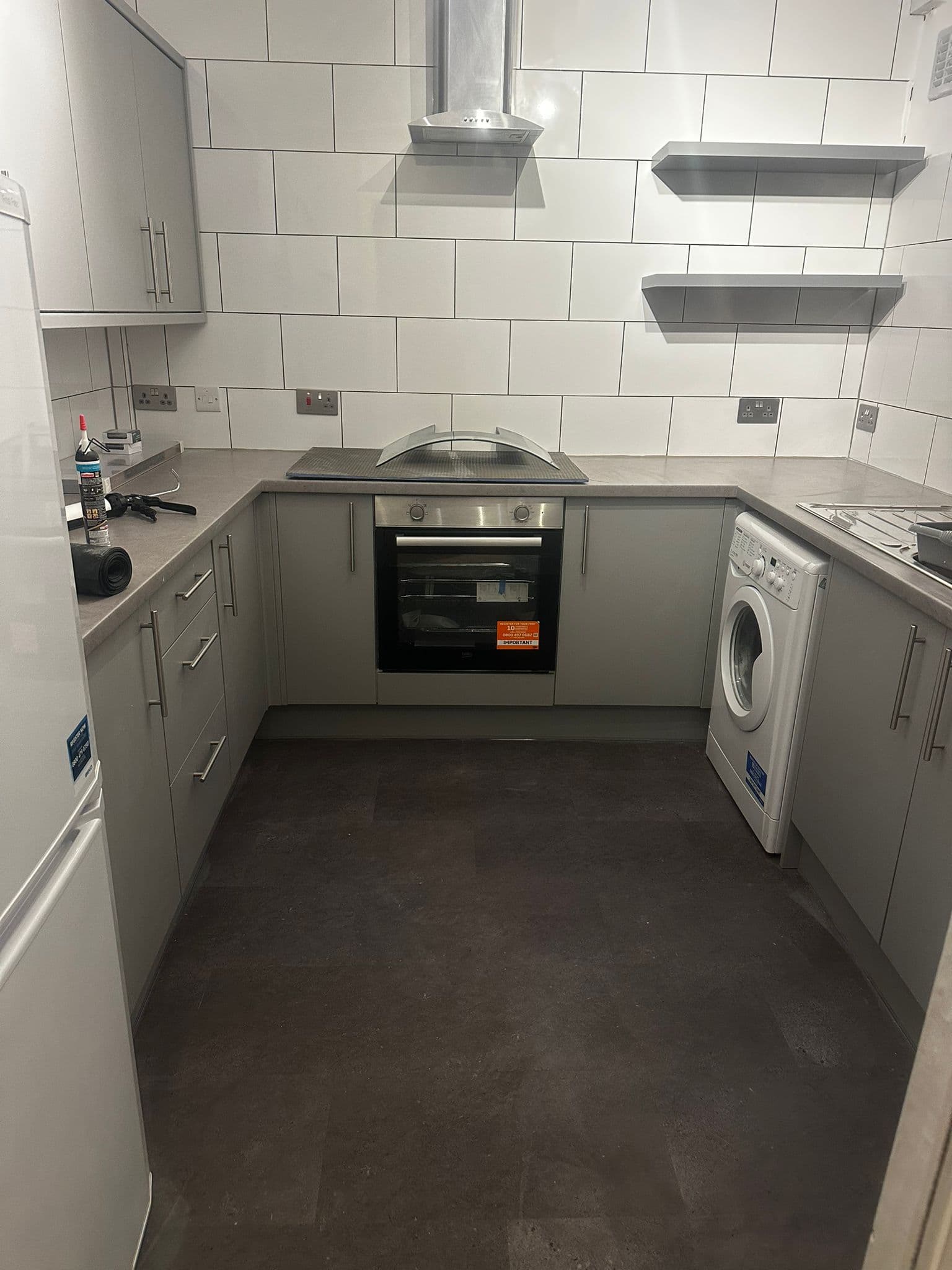 Grey kitchen complete with floating shelves, oven, extractor and white metro tiles