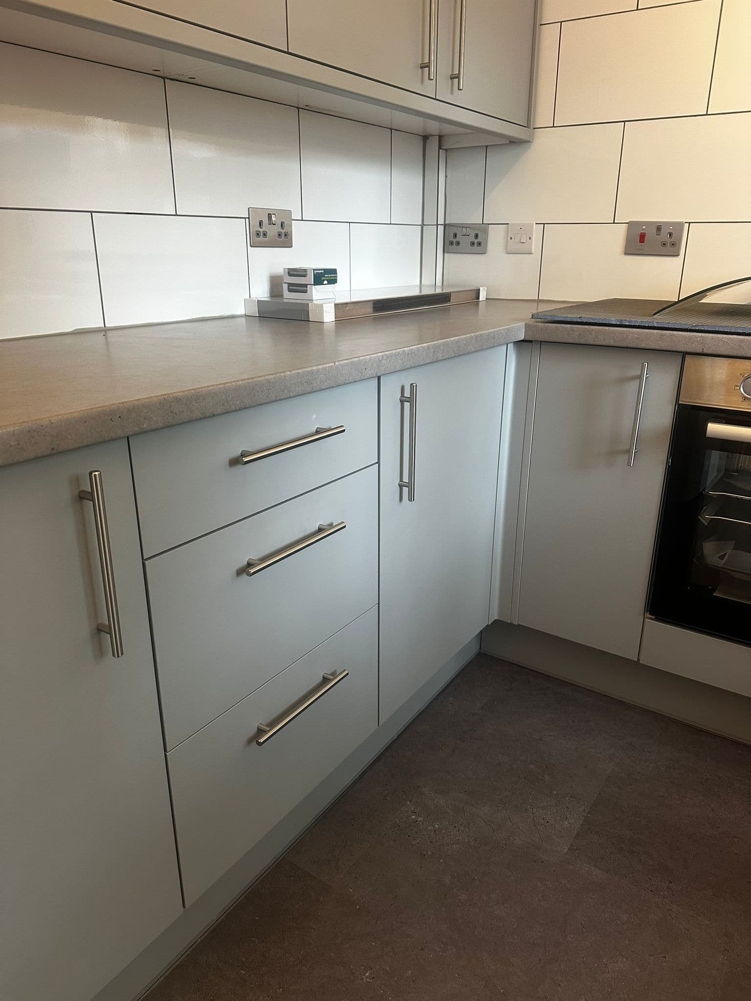 Grey kitchen drawers with brushed steel handles and white tile splashback