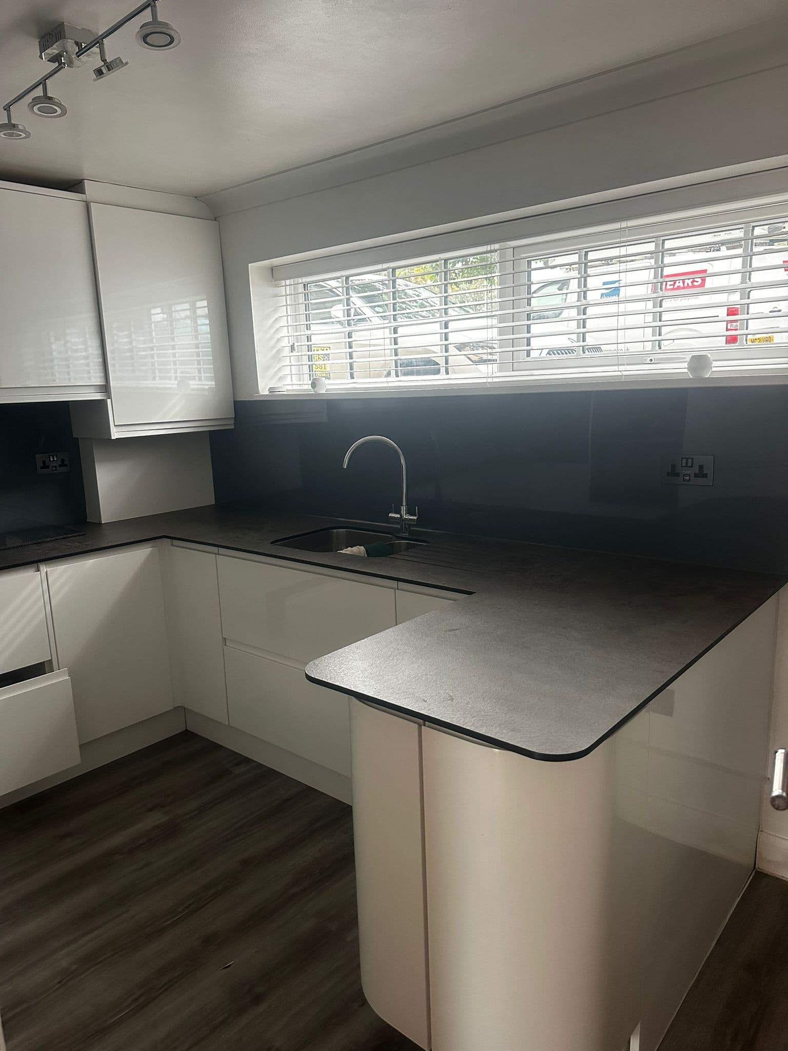 White gloss kitchen with dark countertop, blue glass splashback and breakfast bar