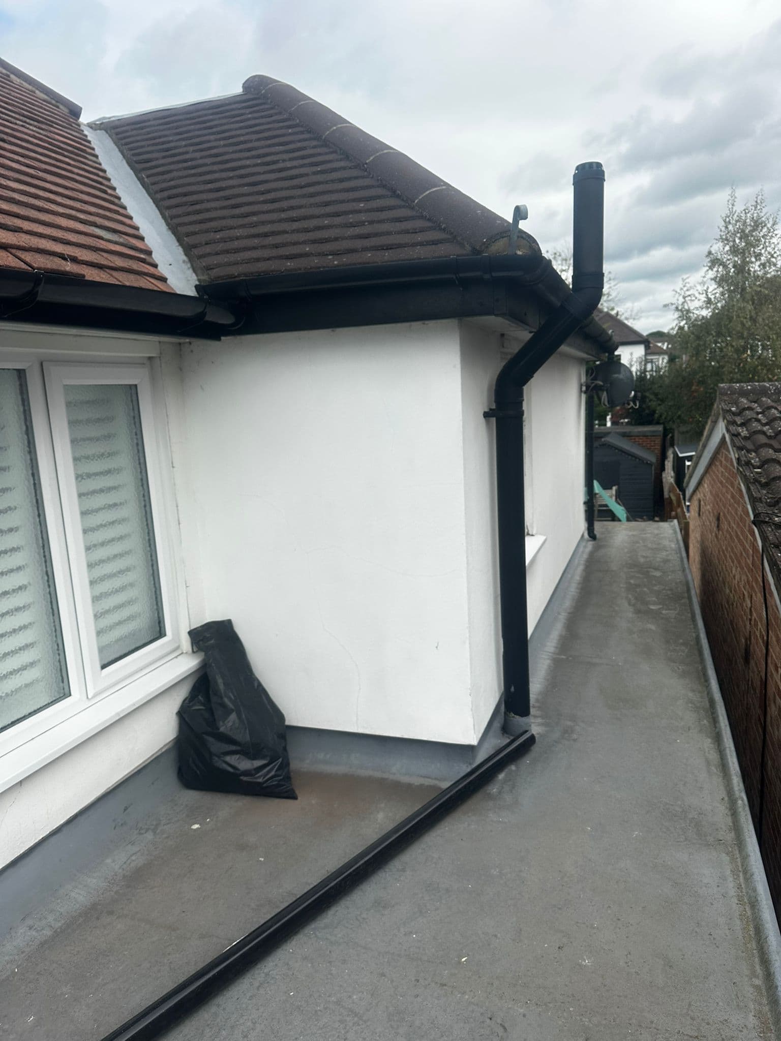 Completed flat roof with black downpipe on white render