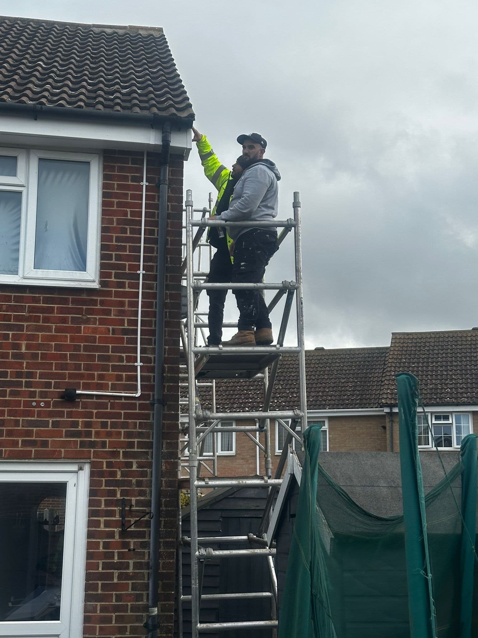 Two workers on scaffold at roofline installing guttering system